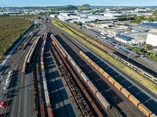 Aerial view of freight trains and cargo containers at a rail yard. Industrial buildings and parked vehicles are visible in the background. Logistics and transportation. PENROSE, AUCKLAND, NZ