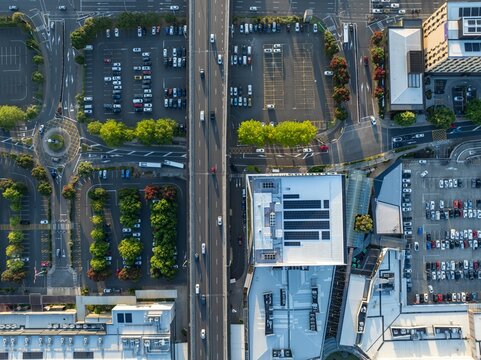 High-angle view of a city parking lot, roads, and buildings. Cars parked, traffic flowing, and solar panels on a building roof. Urban infrastructure. SYLVIA PARK, AUCKLAND, NZ