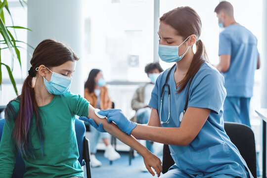 Woman doctor or nurse in protective face mask and gloves preparing to inject patient with flu antiviral vaccine, rubbing hand with cotton pad. Mass vaccination centre, global immunization campaign