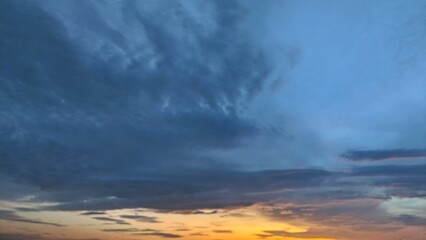 The image captures a breathtaking sunrise sky. The sky is painted with hues of deep blue, transitioning into a vibrant orange and pink near the horizon. Wispy clouds streak across the canvas.