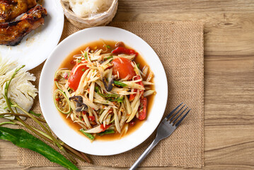 Spicy papaya salad (Som Tum) eating with sticky rice and grilled chicken wing on wooden table, Local Thai food