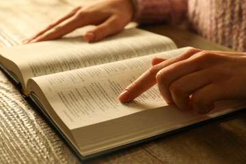 Woman reading Holy Bible in English language at wooden table, closeup