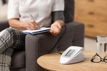 Senior woman writing results of blood pressure measurement at home, closeup