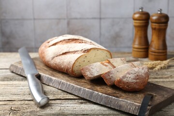 Cutting board with fresh bread, knife, spikes and shakers on wooden table, closeup