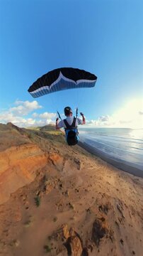 Paraglider soaring fast along the New Zealand coast at sunset. Adventure and freedom concept.