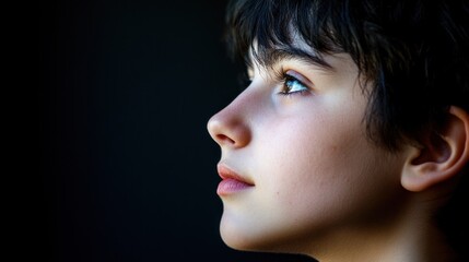 Fototapeta premium Boy gazing upward, profile, indoors, dark background, hope concept