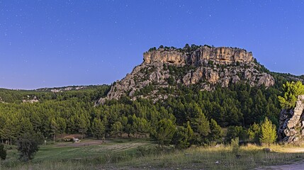 Majestic rocky cliff under a starry sky, surrounded by lush green forests at twilight