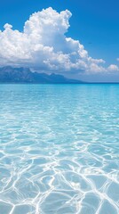Clear turquoise ocean water under a bright blue sky with fluffy clouds and distant mountains