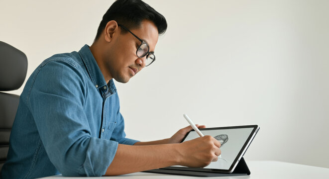 A man wearing glasses is drawing on a tablet