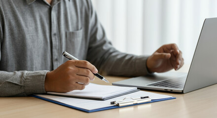A man is sitting at a desk with a laptop and a notebook