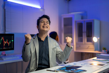 A man in a suit is smiling and celebrating in front of a computer monitor