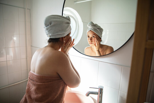 Woman in towel with hair wrap looking at bathroom mirror