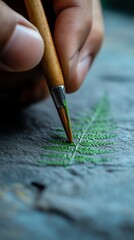 Hand paints fern leaf detail on paper, nature backdrop