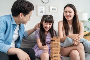 Asian loving parents playing wood block game with young daughter in house.