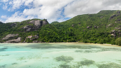 Turquoise lagoon nestled against lush green hills and rocky outcrops. Seychelles. Baie Ternay Marine National Park.