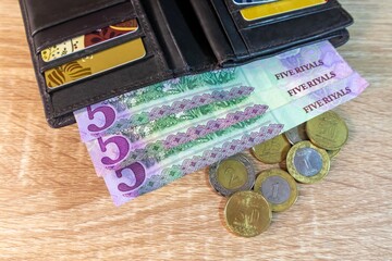 A brown leather wallet on the table with Saudi Arabian Riyal banknotes and coins