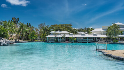 A relaxation area by the swimming pool in a tropical resort hotel. Canopy over turquoise water. Cottages, palm trees, green vegetation, boulders on the shore. The blue sky. Philippines. Cebu.