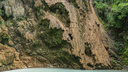 A fragment of a beautiful tropical waterfall. Thin streams of water flow down the mossy terraces of the slope into the turquoise lake. Green vegetation. Philippines. Cebu. Tumalog Falls.