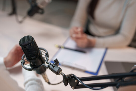 Radio host adjusting the microphone while interviewing a guest in a professional recording studio, with a clipboard and pen resting on the table, creating an engaging atmosphere for discussion