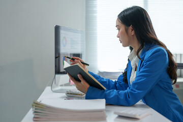Young professional woman in a blue suit working diligently at a computer, analyzing documents and...