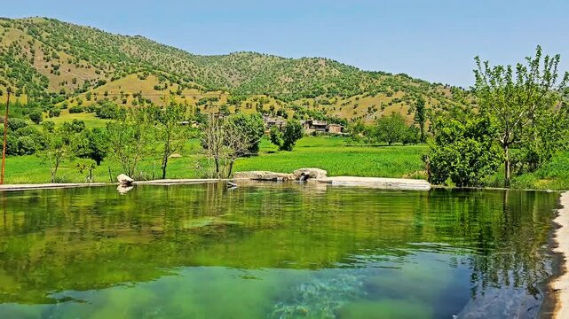 A tranquil pond reflects lush greenery and distant mountains under a clear blue sky.
📍Marivan - Kurdistan 
