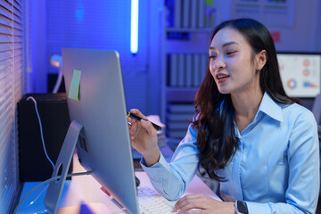 Young professional woman working on a computer in a dimly lit office. She is focused and using a...