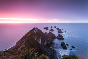 Nugget point lighthouse on a rocky cliff and ocean at dawn, Otago, New Zealand