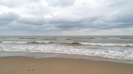 Obraz premium Calm beach scene with rolling waves under a cloudy sky, inviting relaxation and reflection