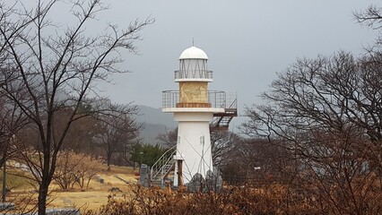 seaside hill with a white watchtower and surrounding trees in korea