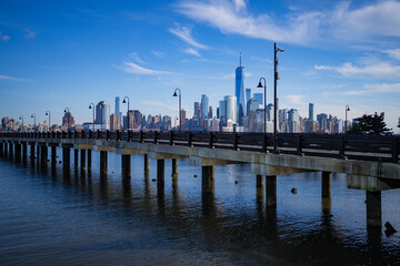 Naklejka premium Lower Manhattan and One World Trade Center in New York City, USA as seen from Weehawken New Jersey. Skyscrapers of Manhattan located near rippling water of New York bay against blue sky.
