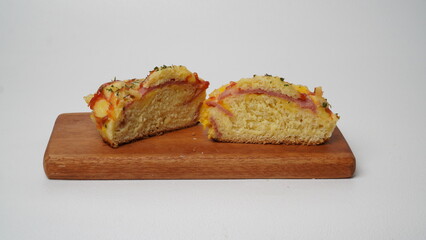 A half salty bread is served in a paper cup with smoked beef filling, orange cheddar and topped with mayonnaise, tomato sauce, and parsley which is placed on a wooden plate with a white background