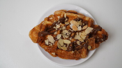 A croffle topped with chocolate jam and a sprinkling of sliced ​​almonds served on a white plate and placed on a white base and background (isolated white).