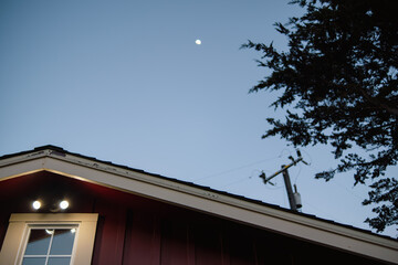 Looking at eves of a red house at dusk with the moon and a power line pole