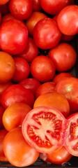 Ripe red tomatoes piled together; some have slight imperfections on the skin; one tomato is cut in half, revealing its interior with seeds and pulp;