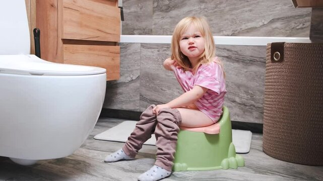 A little child girl is sitting on a potty in the apartment's bathroom. The concept of potty training.