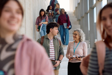 Happy mature teacher talking to student in hallway at university.