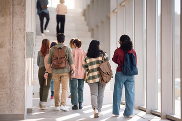 Rear view of college students walking in hallway.