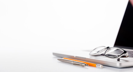 Closeup of an office table featuring a sleek laptop and reading glasses on a clean white surface