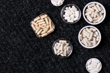 Dietary supplements, many vitamins and minerals in small plates and jars on black background from above. Big amount of white colored pills and nutritional supplements, top view. Healthy lifestyle