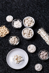 Dietary supplements, many vitamins and minerals in small plates and jars on black background from above. Big amount of white colored pills and nutritional supplements, top view. Healthy lifestyle