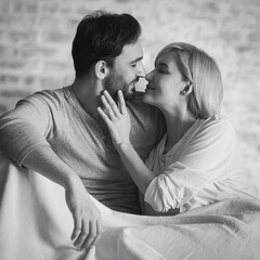 Monochrome bw image - inlove kiss couple with close eyes, lay on home bedroom bed, against bricks wall background. Woman, man at house. Love, relationship, happy family concept
