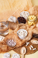 Glass of water, many food supplements in forms of tablets, pills and capsules on beige background in rustic style. Dietary supplements, vitamins and minerals for healthy lifestyle.
