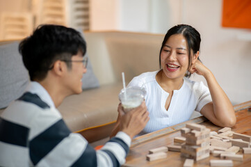 A cheerful, smiling Asian woman enjoys drinks and plays a table game with her boyfriend at home.