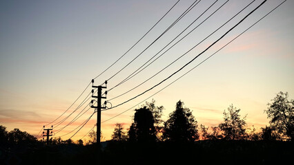 This silhouette scene shows electricity poles and overhead wires stretched across a soft sunset sky. The minimal composition highlights the contrast between manmade infrastructure and the tranquil eve