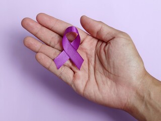 Hands holding Purple ribbons on a purple background. World epilepsy day. Alzheimer's disease, Pancreatic cancer, Epilepsy awareness, fibromyalgia awareness.