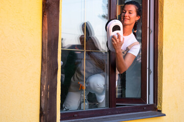 A woman launches window cleaner robot of house outside with a yellow facade. Household robotics, household assistant, cleaning servise