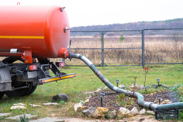 The orange tank of the sewage disposal machine in the courtyard of the house sucks sewage waste...