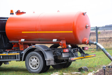 The orange tank of the sewage disposal machine in the courtyard of the house sucks sewage waste from the septic tank well. Waste disposal service, sewage disposal