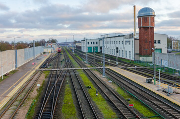 Fototapeta premium Railway station with multiple tracks, train, and historic water tower at dusk. Train station scene, calm atmosphere, wide-angle shot, elevated perspective, industrial setting, multiple railway tracks,