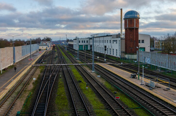 Obraz premium Railway station with multiple tracks, train, and historic water tower at dusk. Train station scene, calm atmosphere, wide-angle shot, elevated perspective, industrial setting, multiple railway tracks,